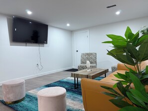 A modern living room with a flat-screen TV mounted on the wall, a patterned armchair, a yellow sofa, a coffee table, and a large green plant. - THE GUEST HOUSE WEST EDMONTON MALL (Edmonton)