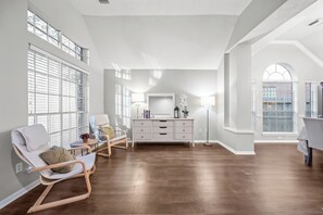 Relax in a spacious room with a high ceiling, large windows, and a comfortable seating area.