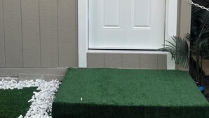A white door with a small window above it, a doorbell, and a green artificial grass step. - Cozy Private Tiny Guest House (Jacksonville)