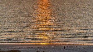 A sunset over a calm sea with a person standing on the beach.