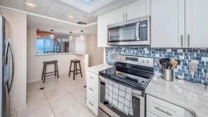 A modern kitchen with white cabinets, a black stove, a microwave, and a tiled backsplash.