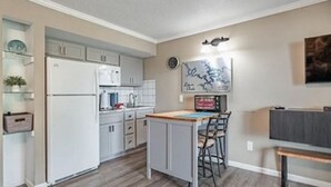A compact kitchen with white cabinets, a refrigerator, and a small island with bar stools.
