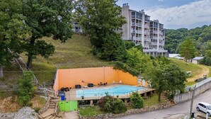 A residential building with a swimming pool, surrounded by greenery and a hillside.