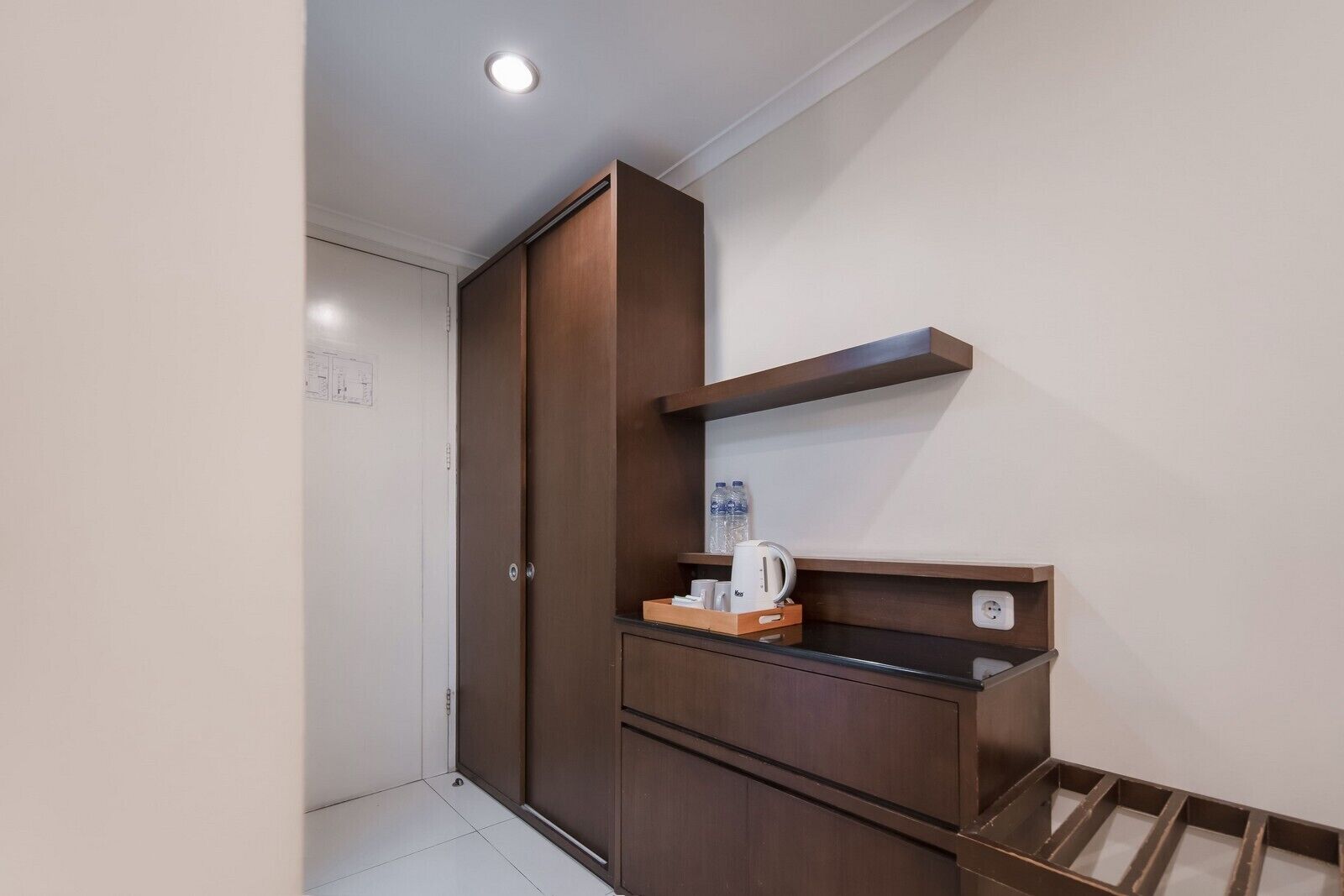 A compact room with a wardrobe, a small shelf with a kettle, and a power outlet.