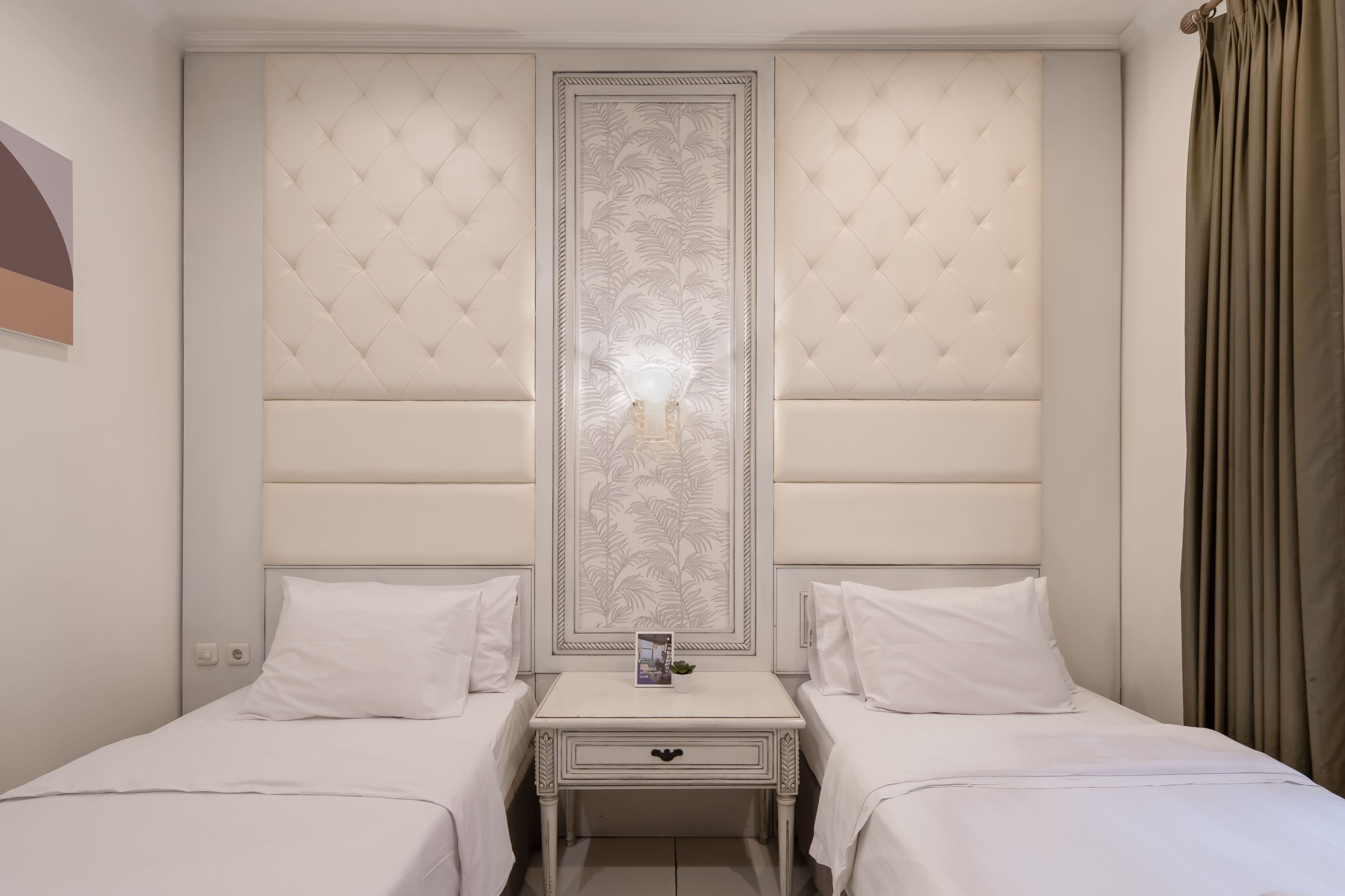 A hotel room with two beds, a nightstand with a lamp, and a decorative panel between the beds.
