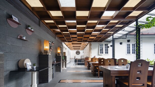 A modern restaurant with a wooden ceiling, black and white walls, and a central dining area with wooden tables and chairs.