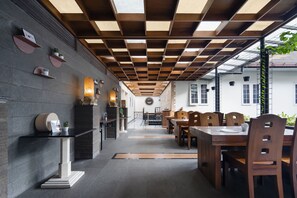 En modern restaurang med ett träpanelat tak, svartvita väggar och en central matsal med träbord och stolar.