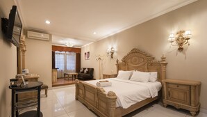 A spacious bedroom with a large bed, bedside tables, a TV, and a desk with a chair.
