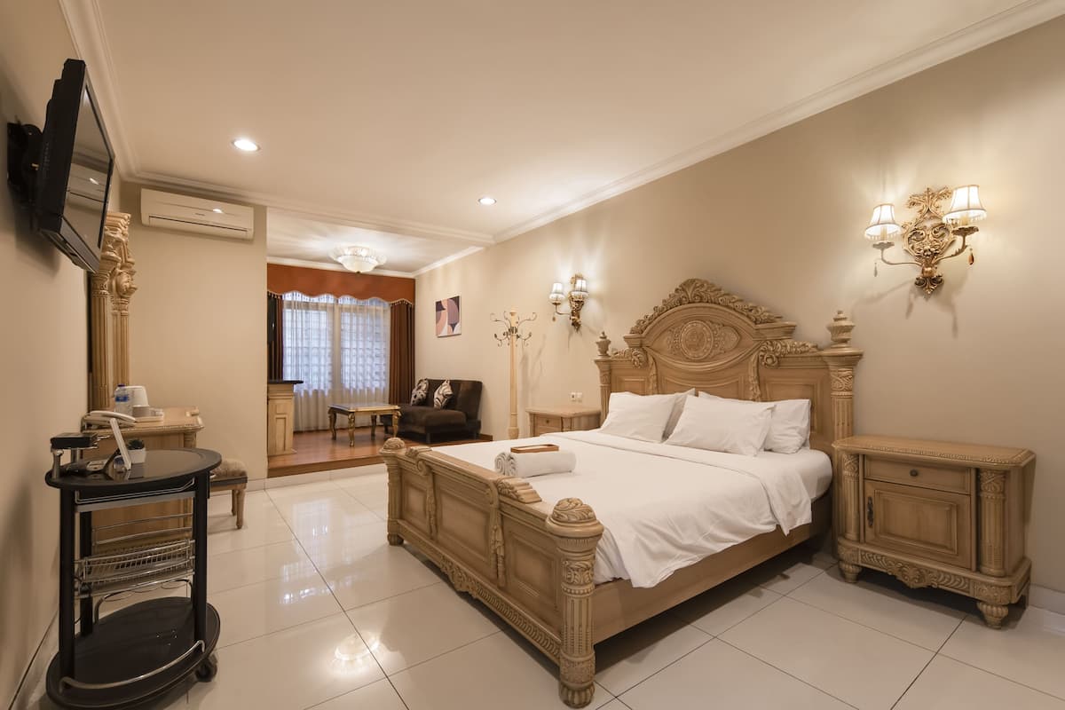 A spacious bedroom with a large bed, bedside tables, a TV, and a desk with a chair.