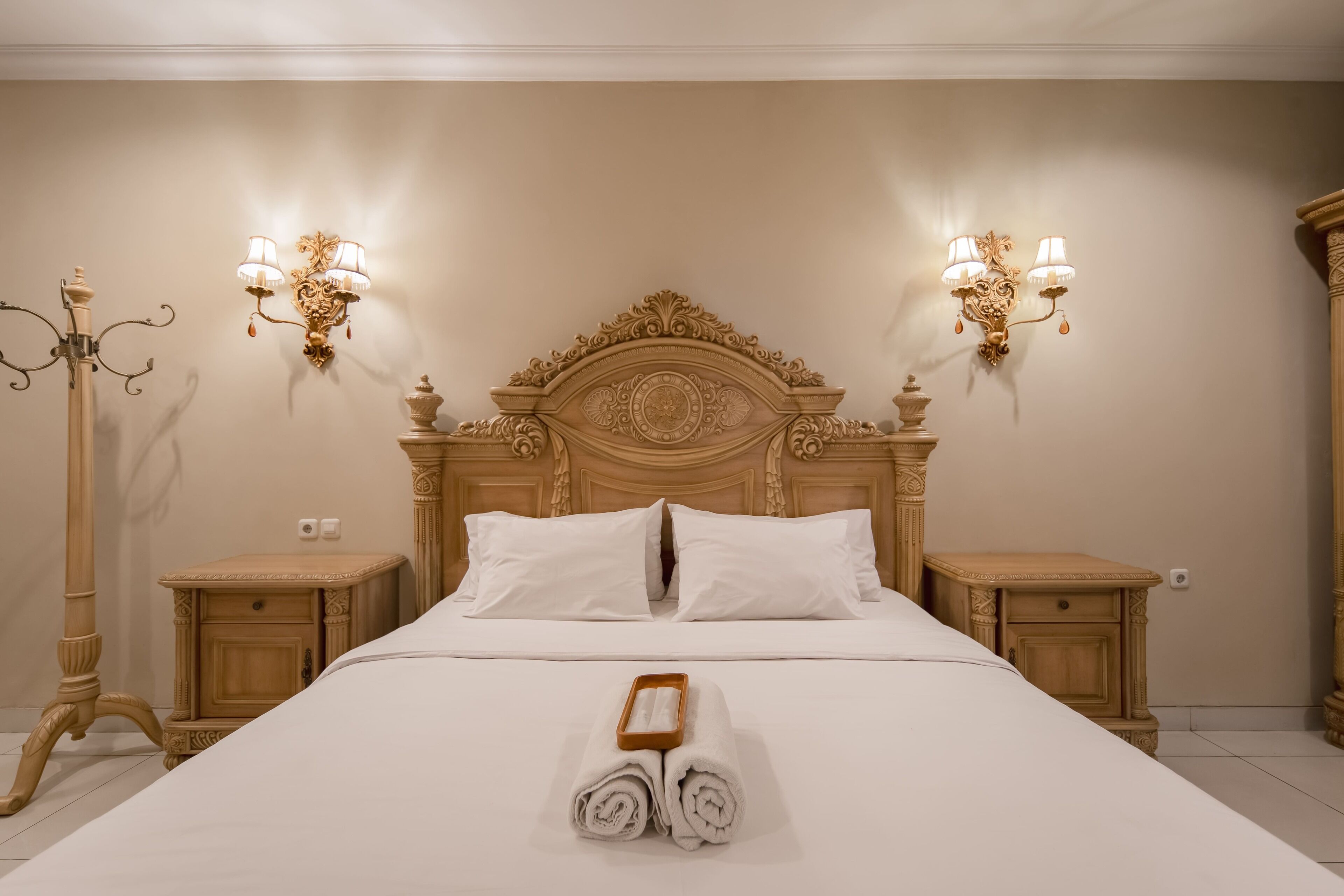 A neatly made bed with white linens, two bedside tables with lamps, and a decorative wall sconce.