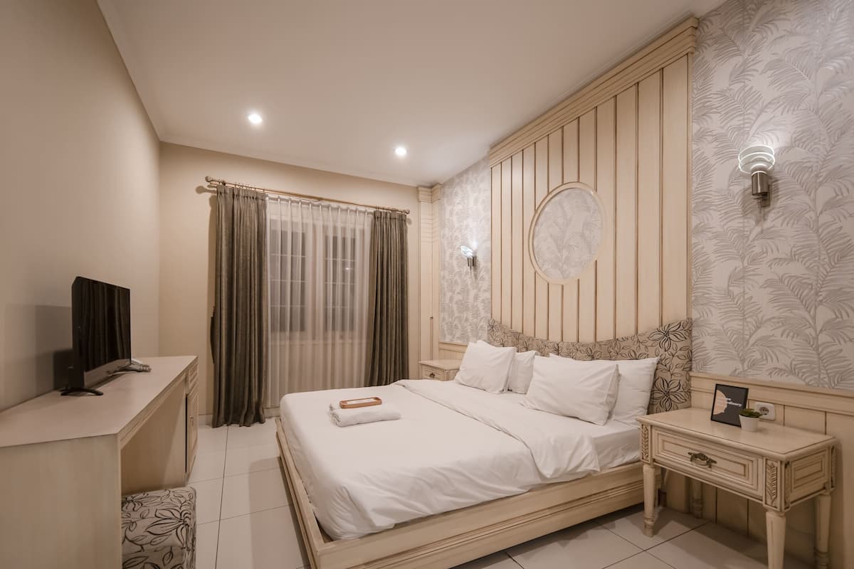 A neatly arranged bedroom with a bed, bedside tables, a desk, and a television.