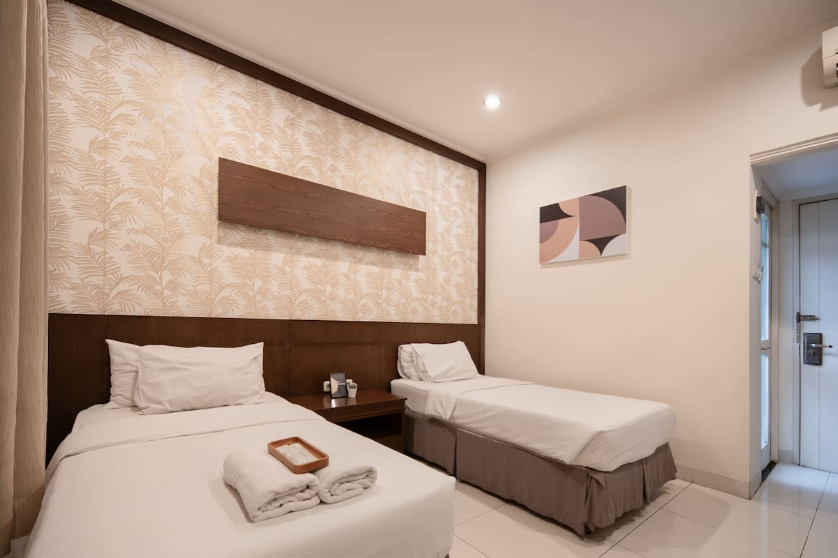 A hotel room with two beds, a wooden headboard, a wall-mounted artwork, and a door.