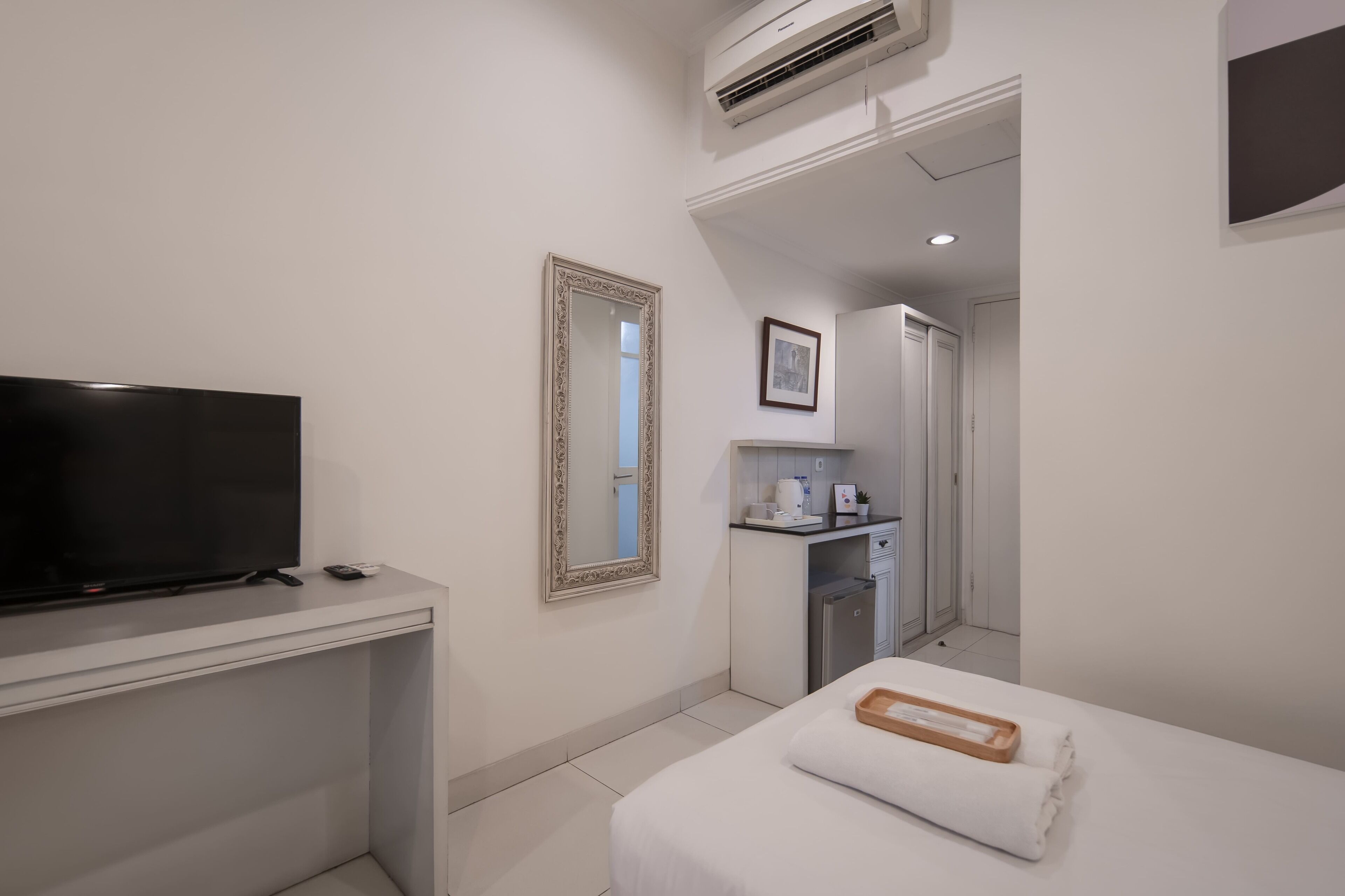 A hotel room with a TV, a bed with a tray, a mirror, a kitchenette, and a door leading to another room.