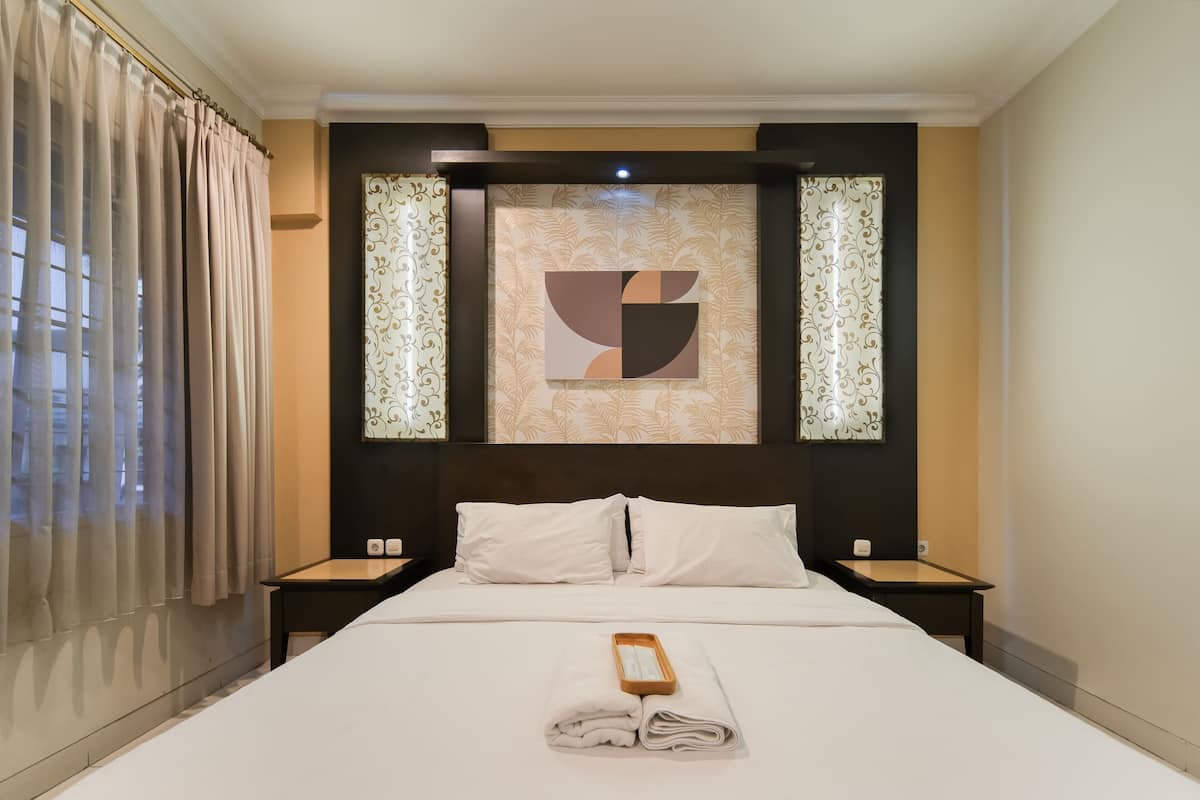 A hotel room with a large bed, two white pillows, a wooden nightstand, and a framed abstract artwork on the wall.