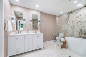 Features a sleek vanity with two sinks and a bathtub.