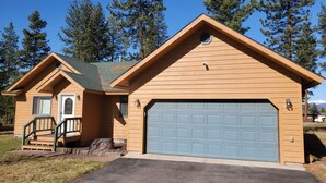 Eine zweistöckige Holzhütte mit Garage, umgeben von hohen Kiefern.