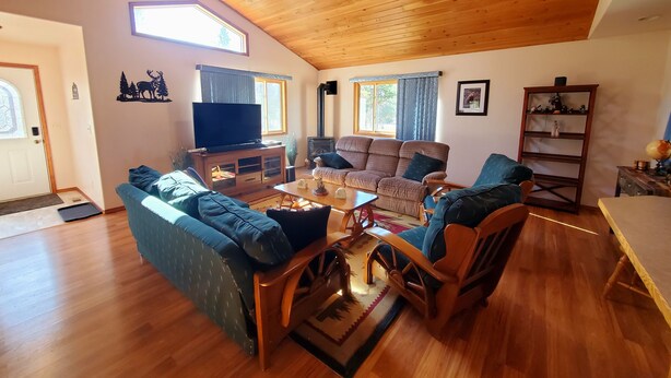 Ein geräumiges Wohnzimmer mit Holzbalkendecke, einem großen Fernseher, einem Kamin und einer gemütlichen Sitzecke.