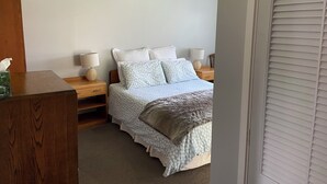 A bedroom with a bed, bedside tables, lamps, a wooden dresser, and a window with blinds. - Cozy, comfortable and close to CBD (Whakatane)