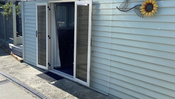 A motel with a sliding glass door entrance, a welcome sign with a sunflower decoration, and a metal awning above the door. - Cozy, comfortable and close to CBD (Whakatane)