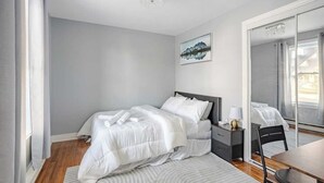 A bedroom with a bed, bedside table, chair, and a large mirror.
