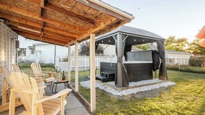 A covered outdoor seating area with wooden chairs and a table, a barbecue grill, and a pergola structure.