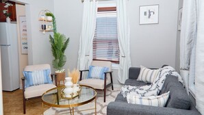A living room with a sofa, two chairs, a coffee table, a plant, and a window with curtains.