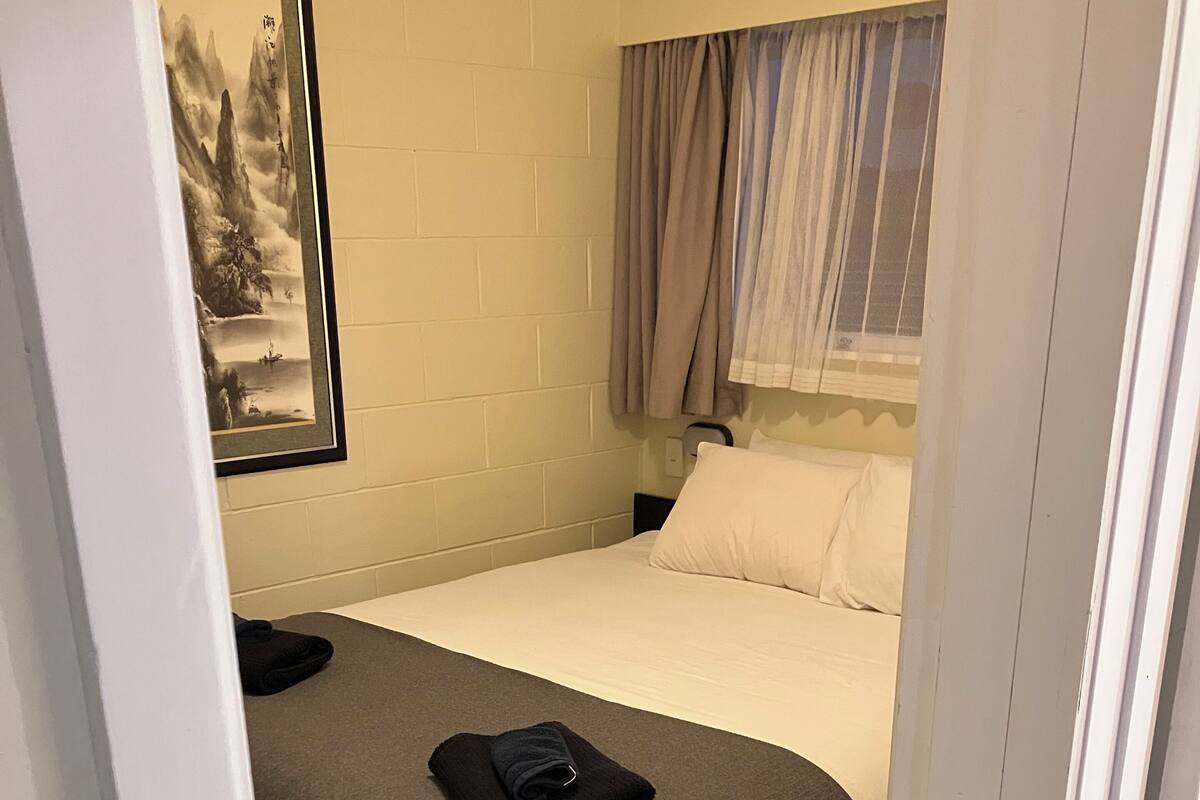 A hotel room with a bed, a nightstand, a framed picture on the wall, and a window with curtains.
