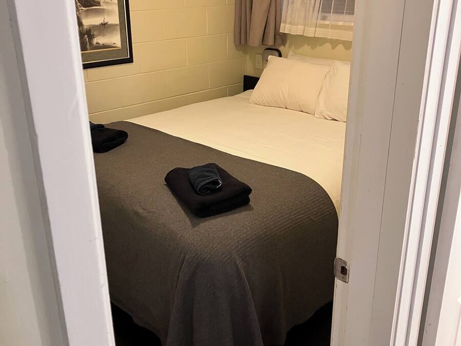 A hotel room with a bed, a nightstand, a framed picture on the wall, and a window with curtains.