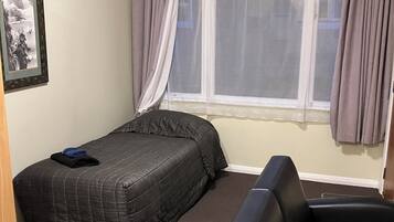 A room with a bed, a chair, a window with curtains, and a framed picture on the wall.