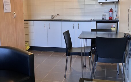 A modern kitchen with white cabinets, a stainless steel range hood, a microwave, and a fire extinguisher. There is a dining area with a table and chairs.