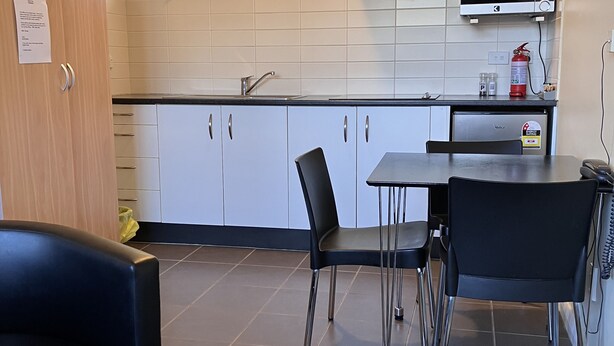 Une cuisine moderne avec des armoires blanches, une hotte de cuisinière en acier inoxydable, un four à micro-ondes et un extincteur. On y trouve également un coin repas avec une table et des chaises.