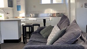 Une pièce compacte et bien éclairée, dotée d’une kitchenette, d’un lit avec une literie grise et d’une petite table.