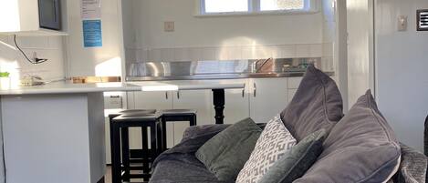 A compact, well-lit room with a kitchenette, a bed with grey bedding, and a small table.