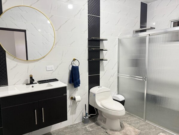 A modern bathroom with a white sink, black cabinets, a toilet, and a glass shower enclosure.