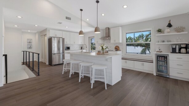 A modern kitchen with a central island, stainless steel appliances, and a large window providing a view of the outdoors. - Luxury Beach Home•Steps to Beach•Excellent Location•Sunsets (Holmes Beach)