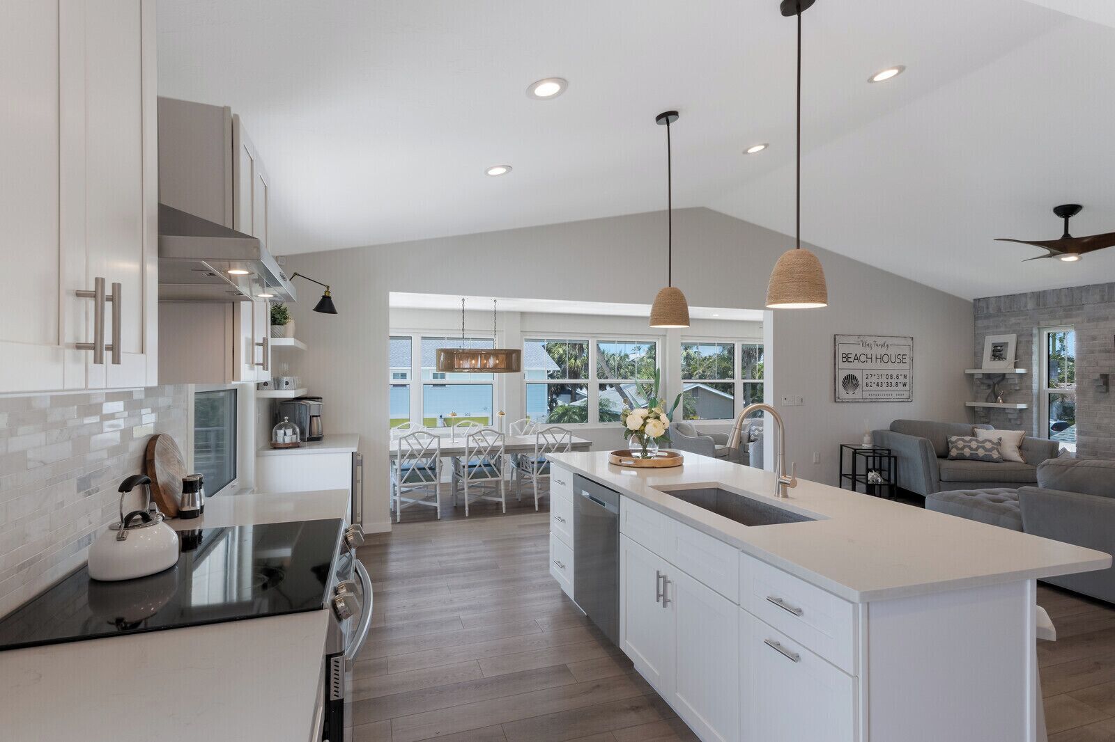 Cozinha moderna com armários brancos, uma ilha central, iluminação pendente e vista para o exterior.