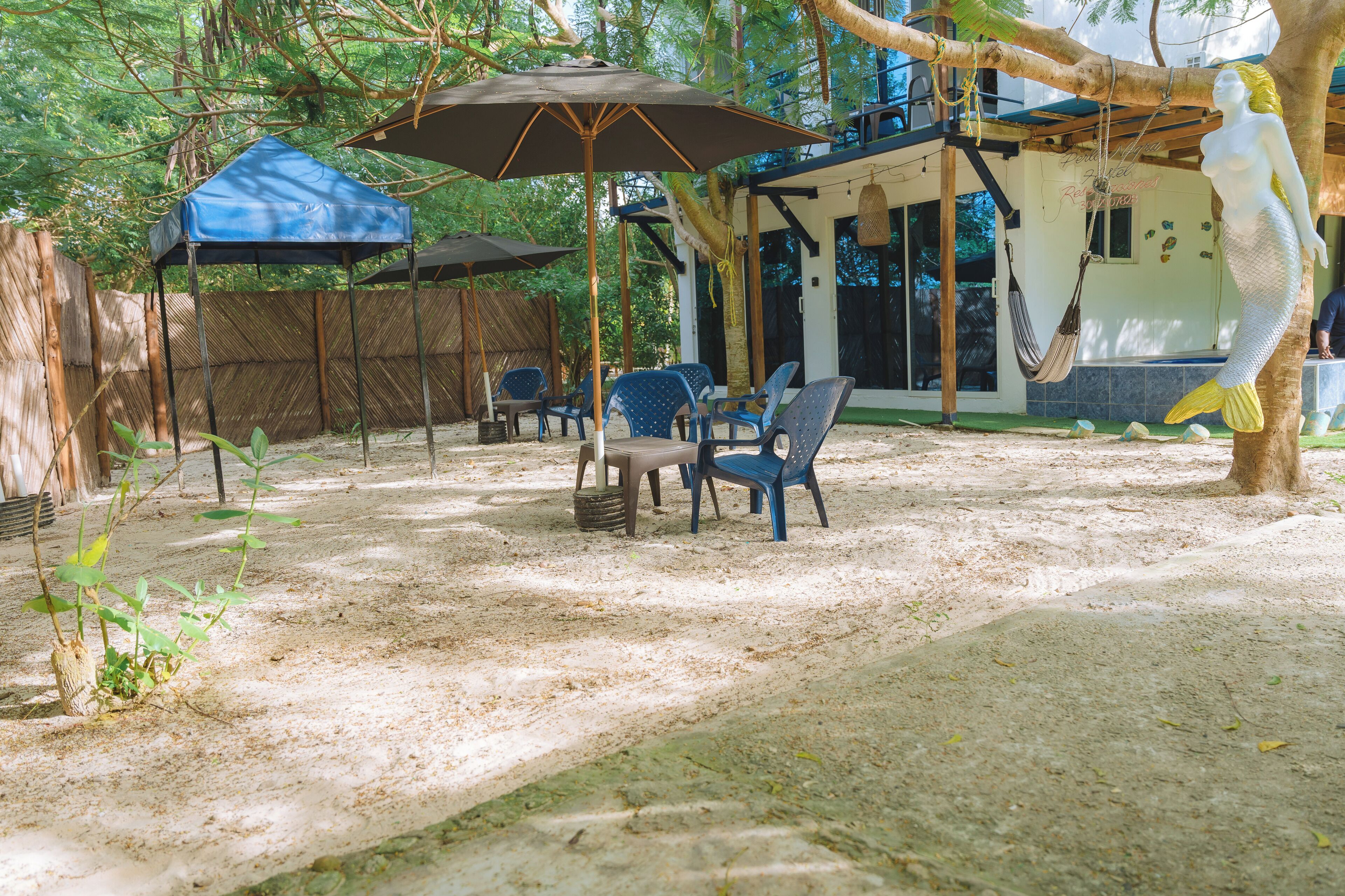 Un espace extérieur aménagé avec des chaises bleues et une table, entouré d’arbres et recouvert d’une sorte de tonnelle bleue.