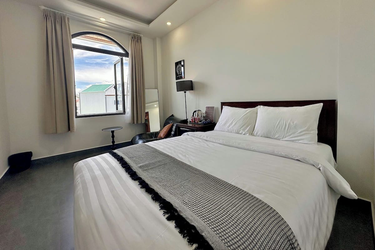 A hotel room with a large bed, a small table, a lamp, and a view of the outside.