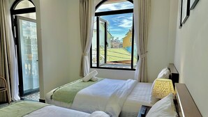 A hotel room with two beds, a window with curtains, a view of the outside, and a small table with a lamp. - Amelia House - Boutique Hotel (Lam Vien - Da Lat)