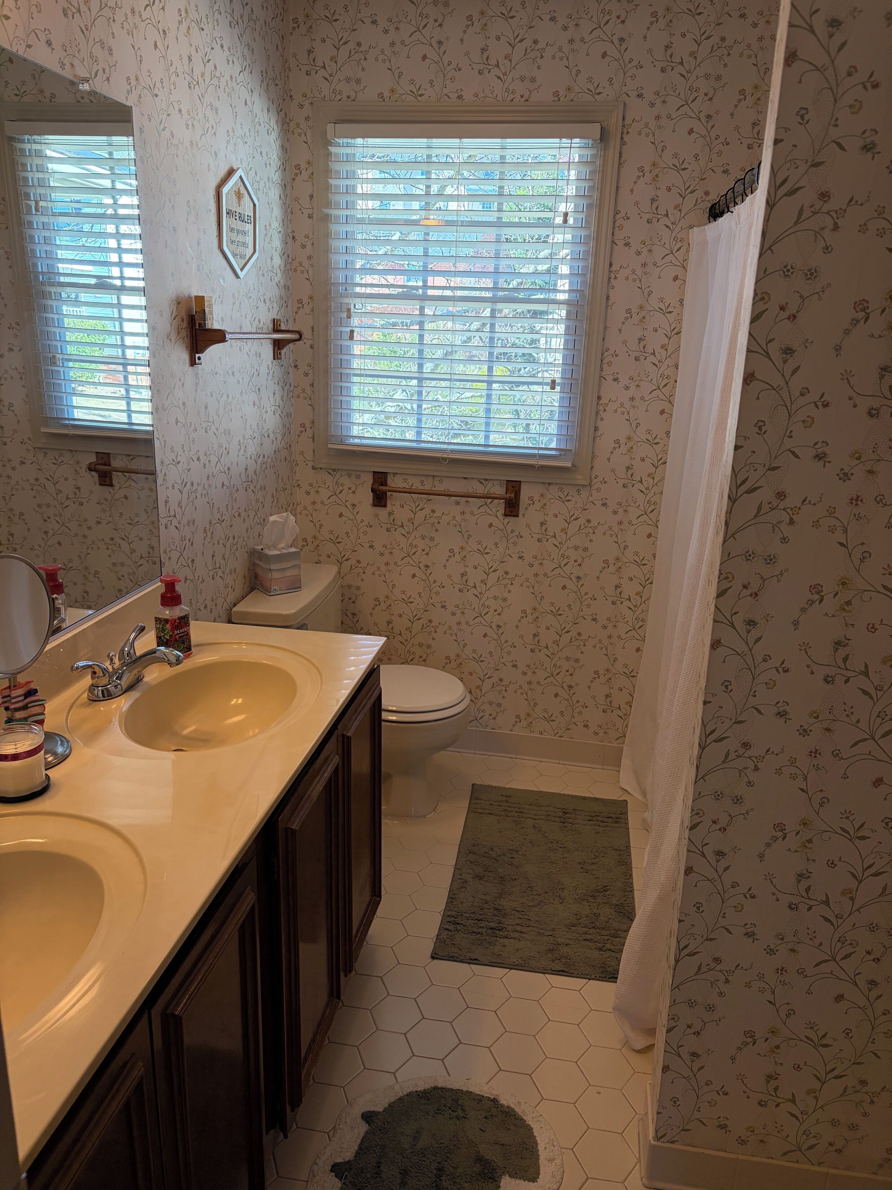 A bathroom with two sinks, a toilet, a shower with a curtain, and a window with blinds.