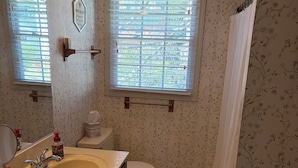 A bathroom with two sinks, a toilet, a shower with a curtain, and a window with blinds.