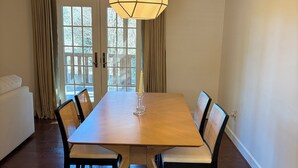 A dining room with a wooden table, black chairs, a hanging light fixture, and a view through a glass door.