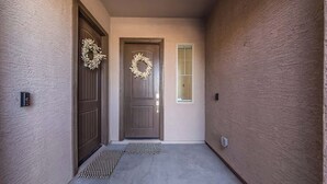 Ein Flur mit zwei Türen, eine mit einem Kranz, einem Fenster mit Rollläden und einer Fußmatte.