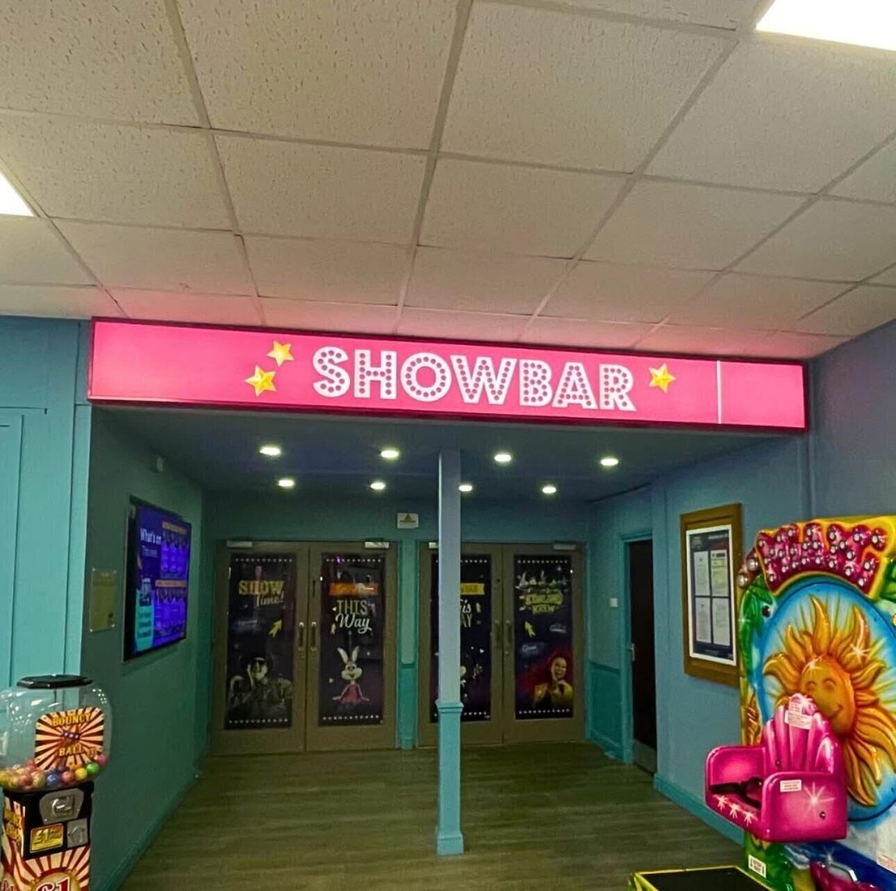 Entrada a un showbar con un letrero de neón, máquinas expendedoras y coloridas decoraciones en la pared.