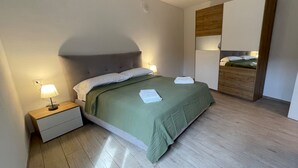 Siististi pedattu sänky, jossa on vihreä päiväpeite, yöpöytälamppu ja puinen yöpöytä.