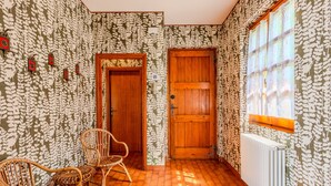 A room with patterned wallpaper, a wooden door, a wicker chair, and a radiator. - Papandrea by Interhome (Brenzone)