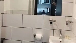 Une salle de bain moderne avec des carreaux blancs, un lavabo et un miroir qui reflète une partie de la cuisine.