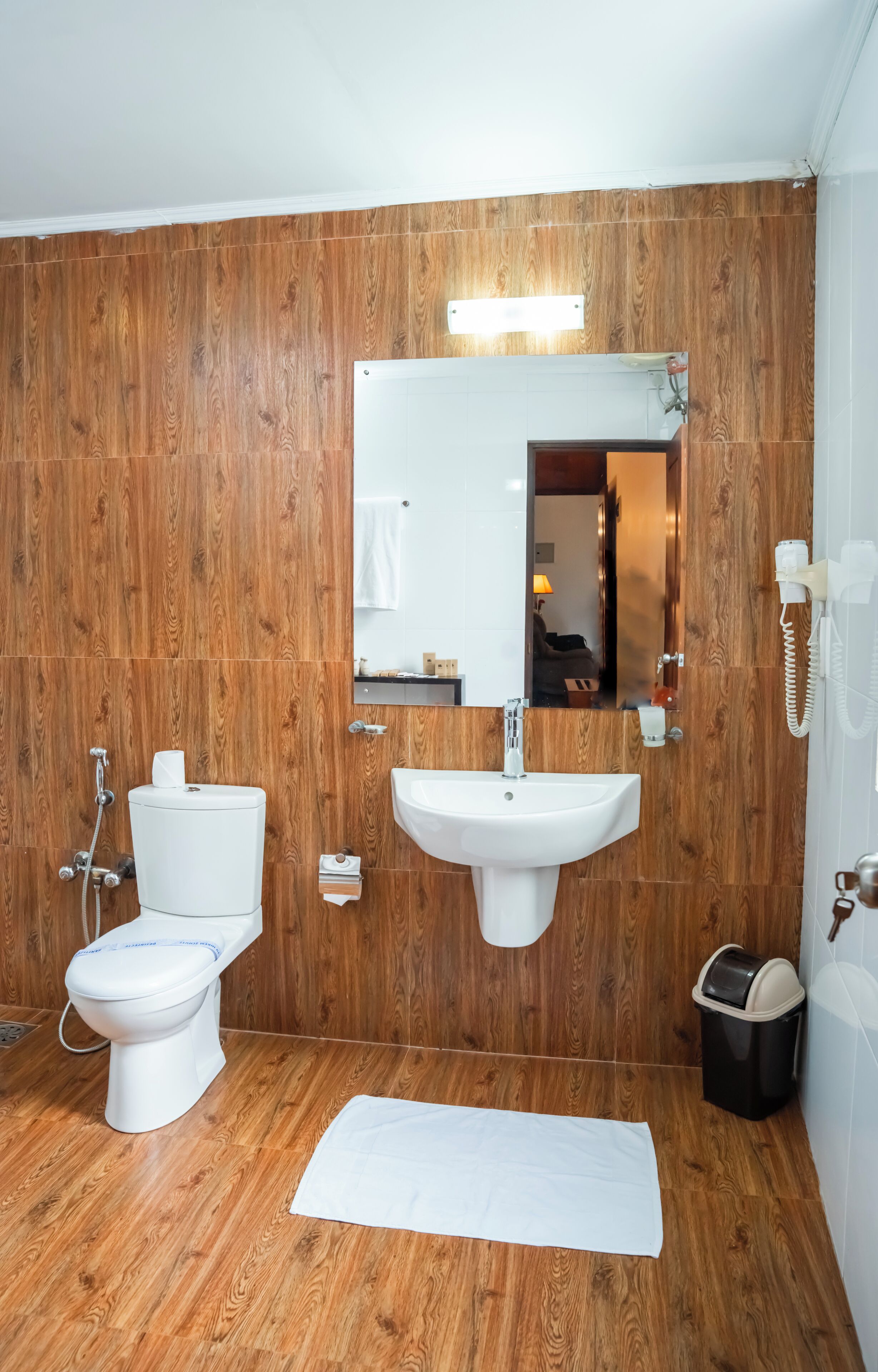 Un baño con paneles de madera, inodoro blanco, lavabo y espejo.