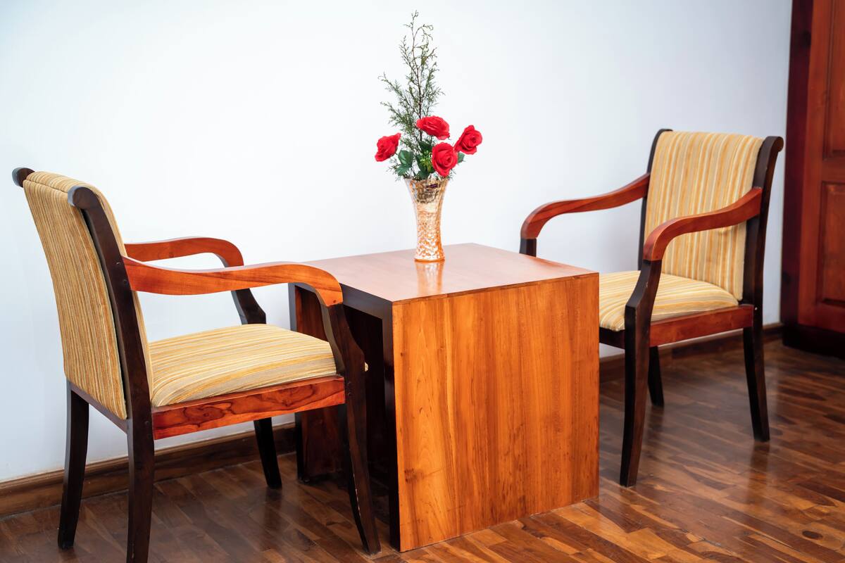Een houten tafel met twee stoelen, een vaas met rode bloemen en een houten vloer.