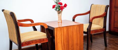A wooden table with two chairs, a vase with red flowers, and a wooden floor.